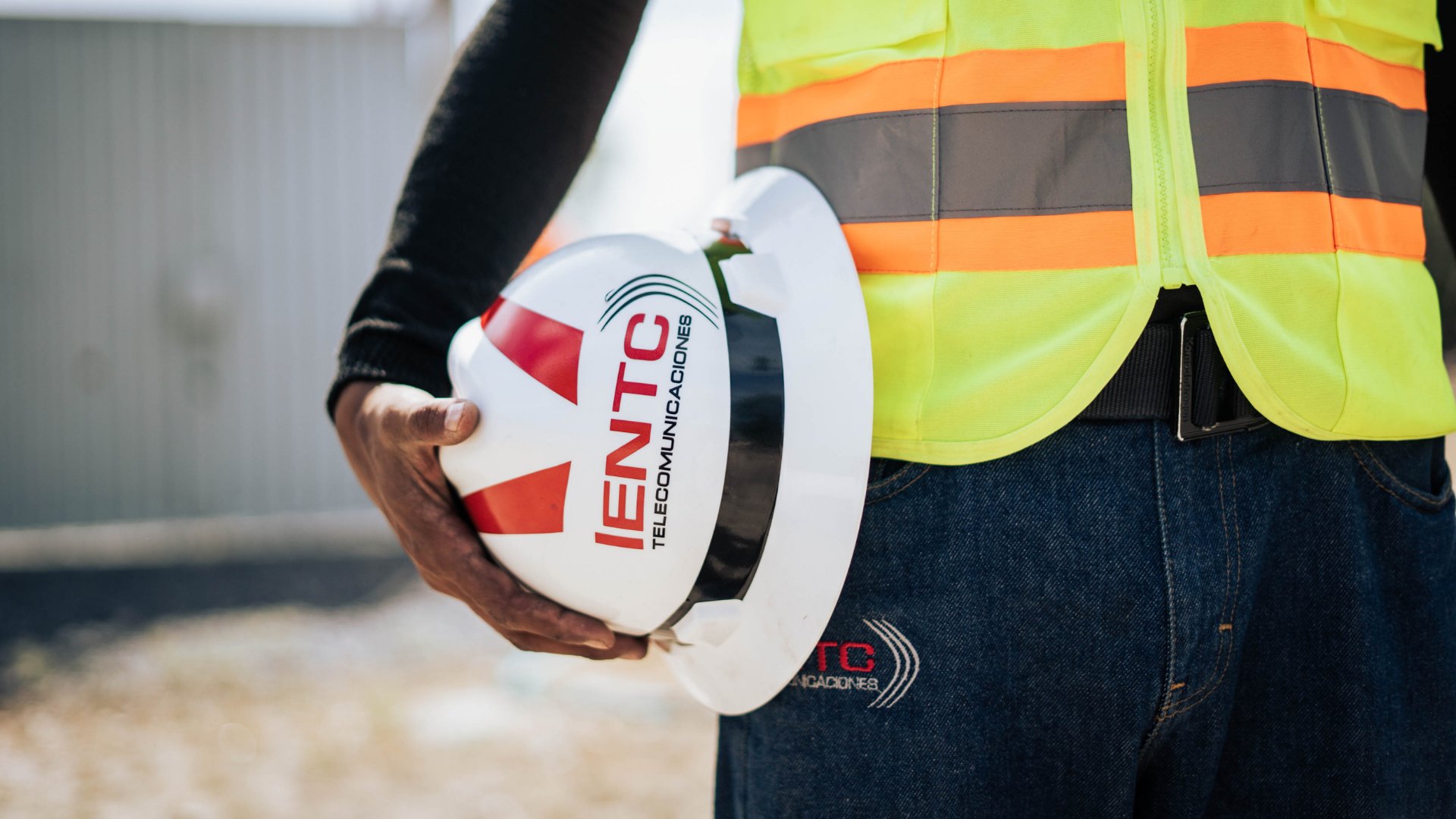 Trabajador de IENTC con chaleco de seguridad sosteniendo un casco blanco con el logotipo de la empresa.